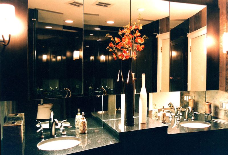 Dark vanity with black stone countertops and a mirrored wall reflecting lights