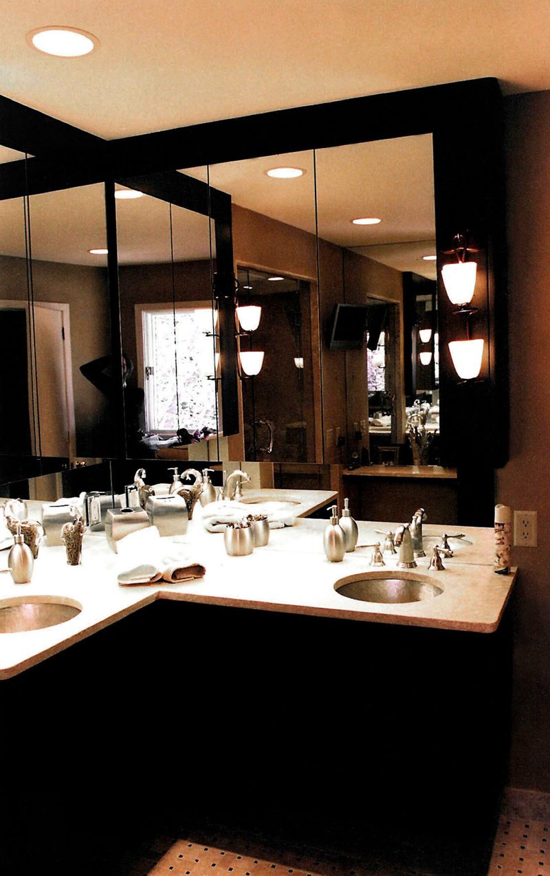Corner double vanity with a white countertop, dark base, and mirrored walls