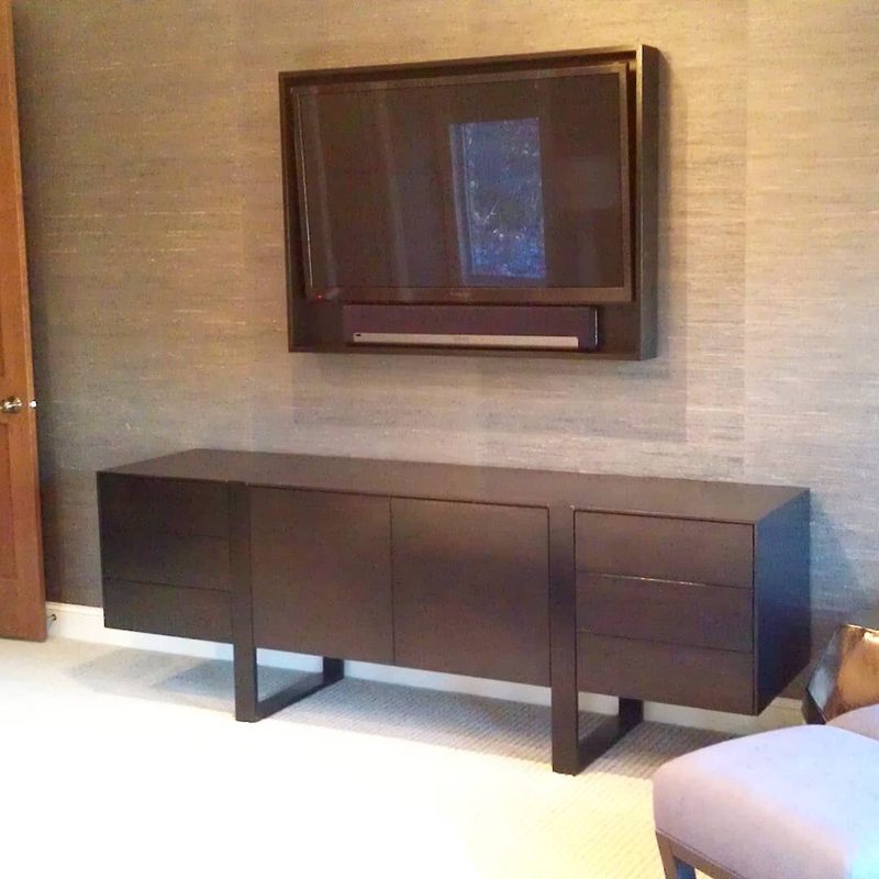 Dark wood low media console on sled legs below a framed wall-mounted TV