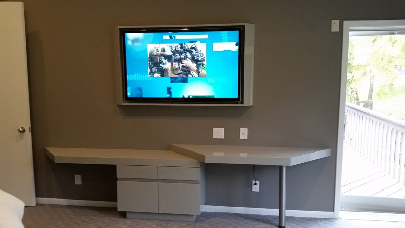 Wall-mounted TV above a floating gray desk with a drawer cabinet