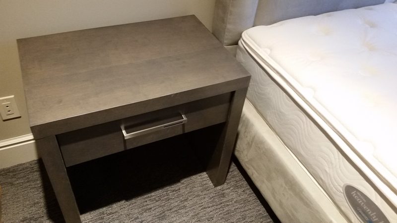 Dark gray nightstand with a single drawer and open base next to a mattress