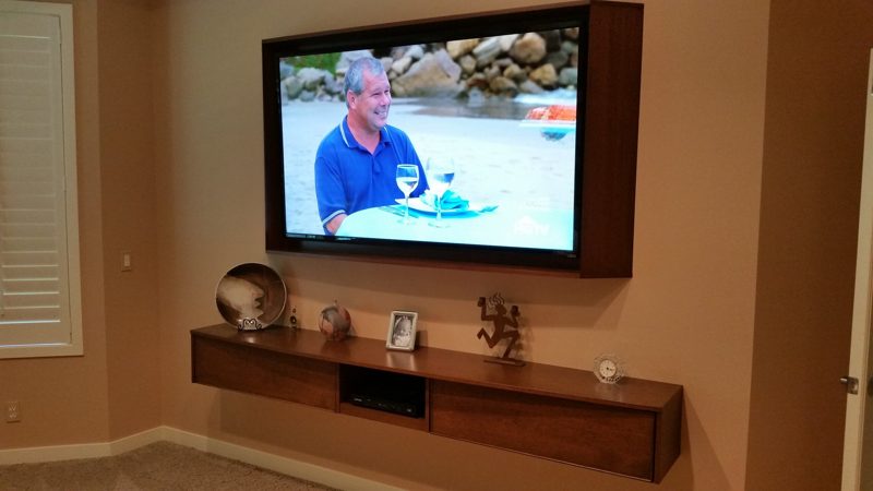 Floating wood media shelf and framed TV with decor on an orange wall