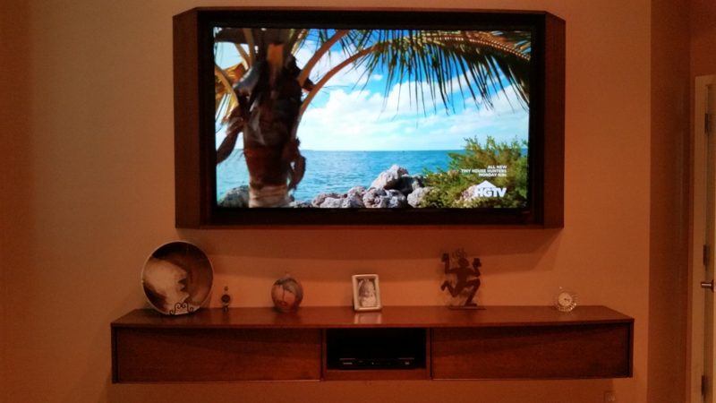 Floating wood media shelf below a framed wall-mounted TV on an orange wall