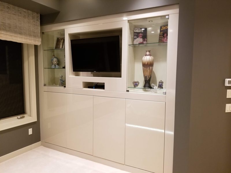 Cream built-in wall unit with a TV, lit glass shelves, and lower doors