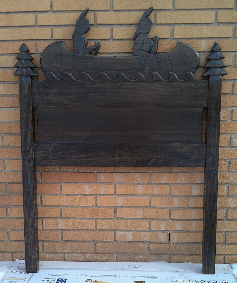 Dark wood twin headboard topped with a cutout of canoe paddlers