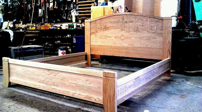 Unfinished light wood bed frame with a carved arched headboard in the shop