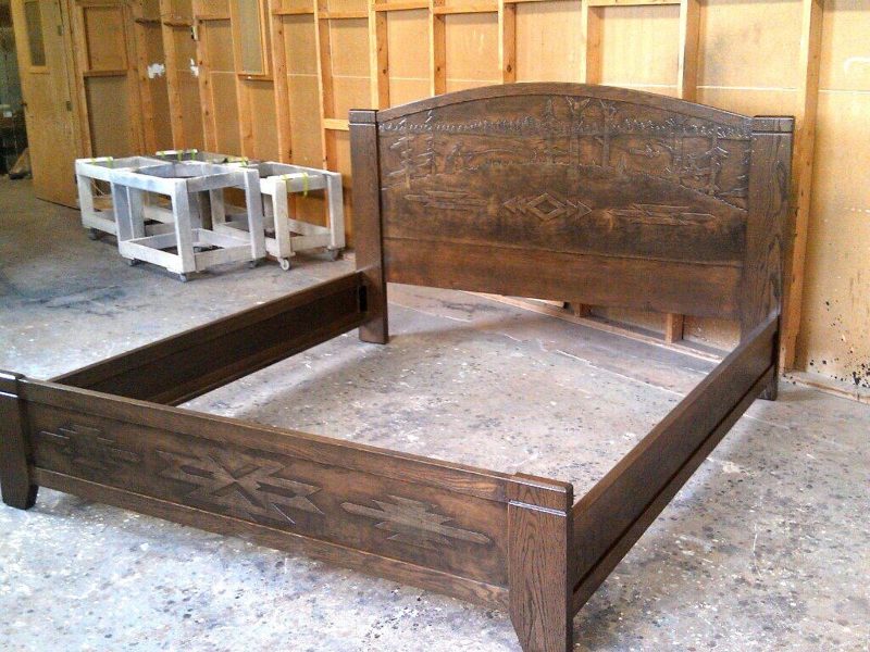 Dark stained bed frame with a carved arched headboard in the shop