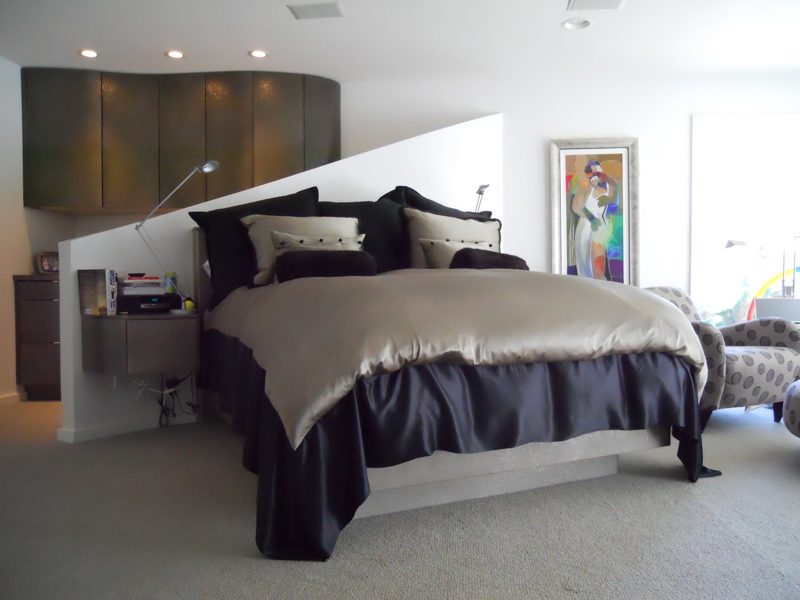 Bed with a gray padded headboard wall and cabinets in an open bedroom