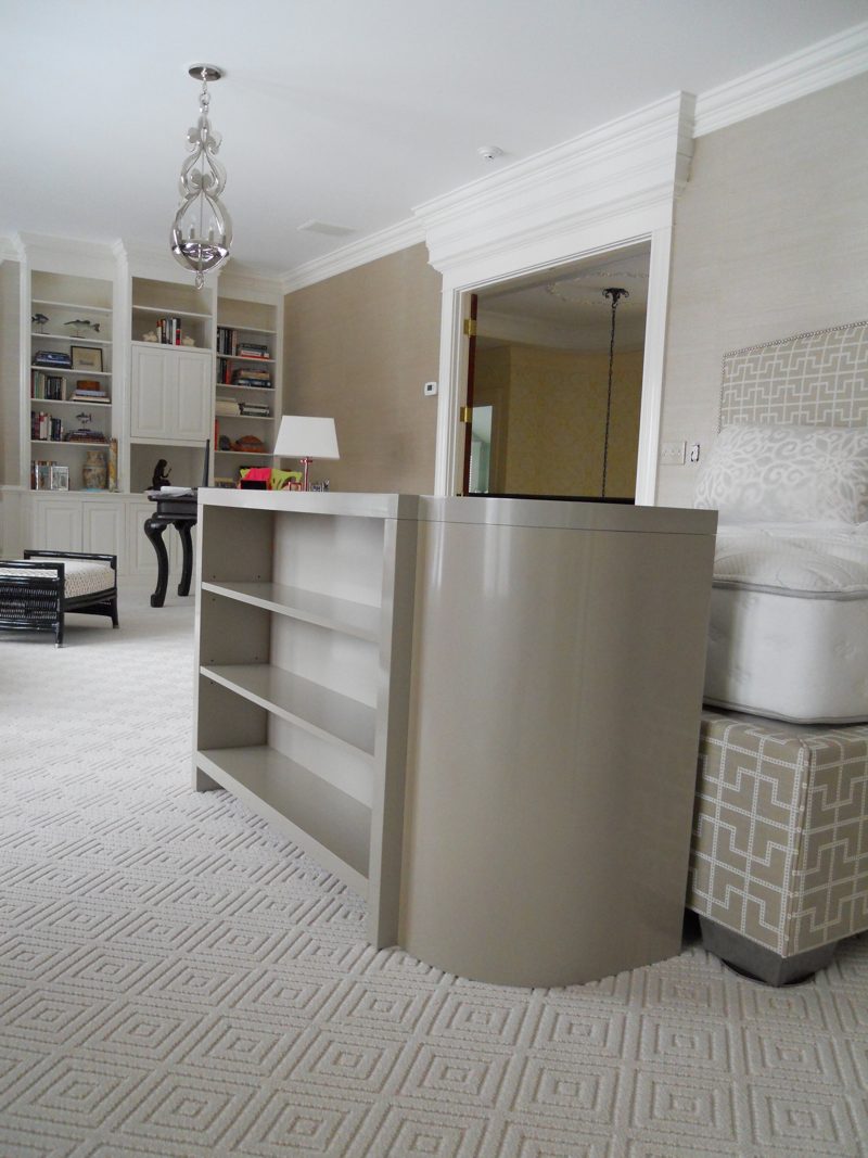 Gray curved TV lift cabinet with open shelves at the foot of a bed