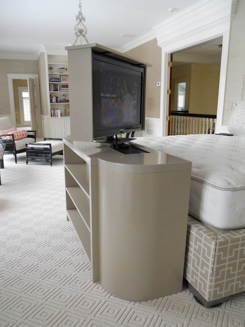 Gray TV lift cabinet at the foot of a bed with the TV raised