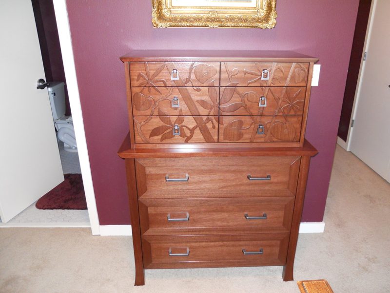 Front view of a reddish wood chest with carved leaf and vine drawers