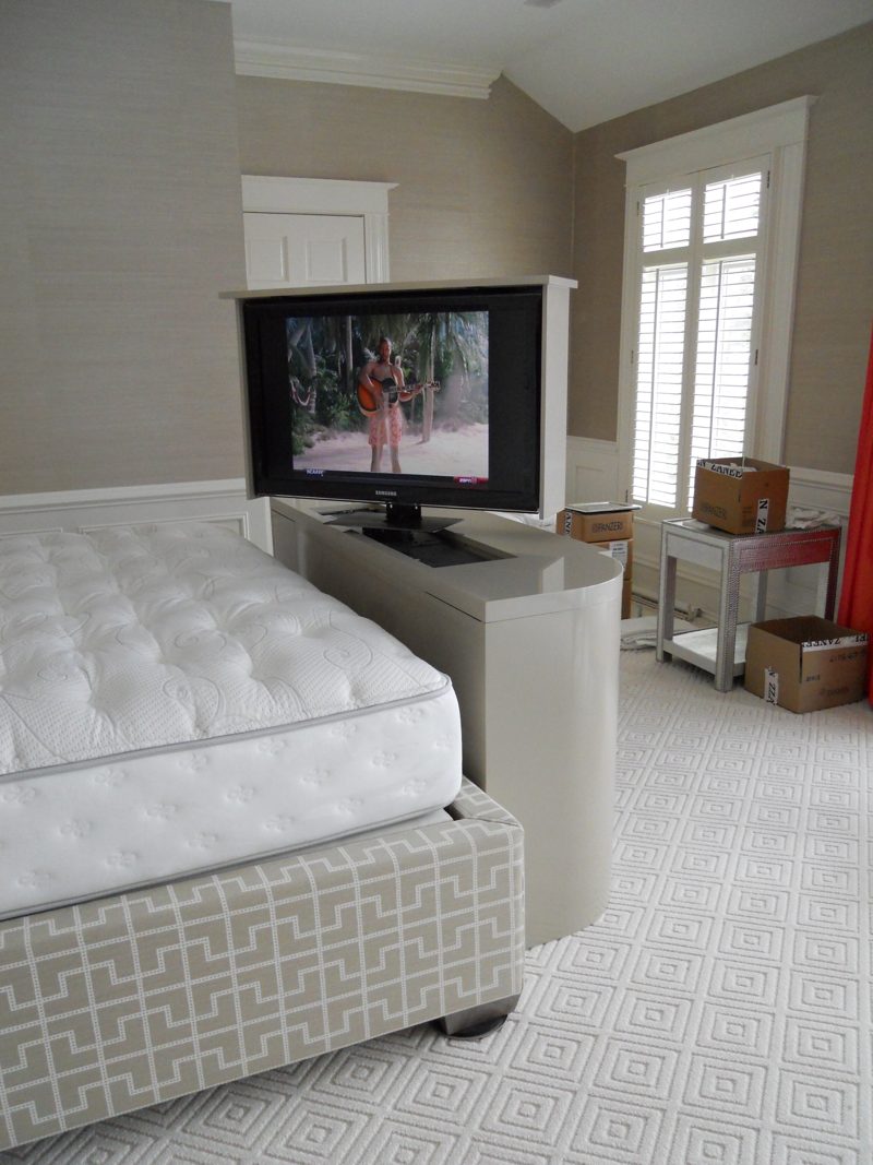 Gray TV lift cabinet with a raised TV seen from beside the bed