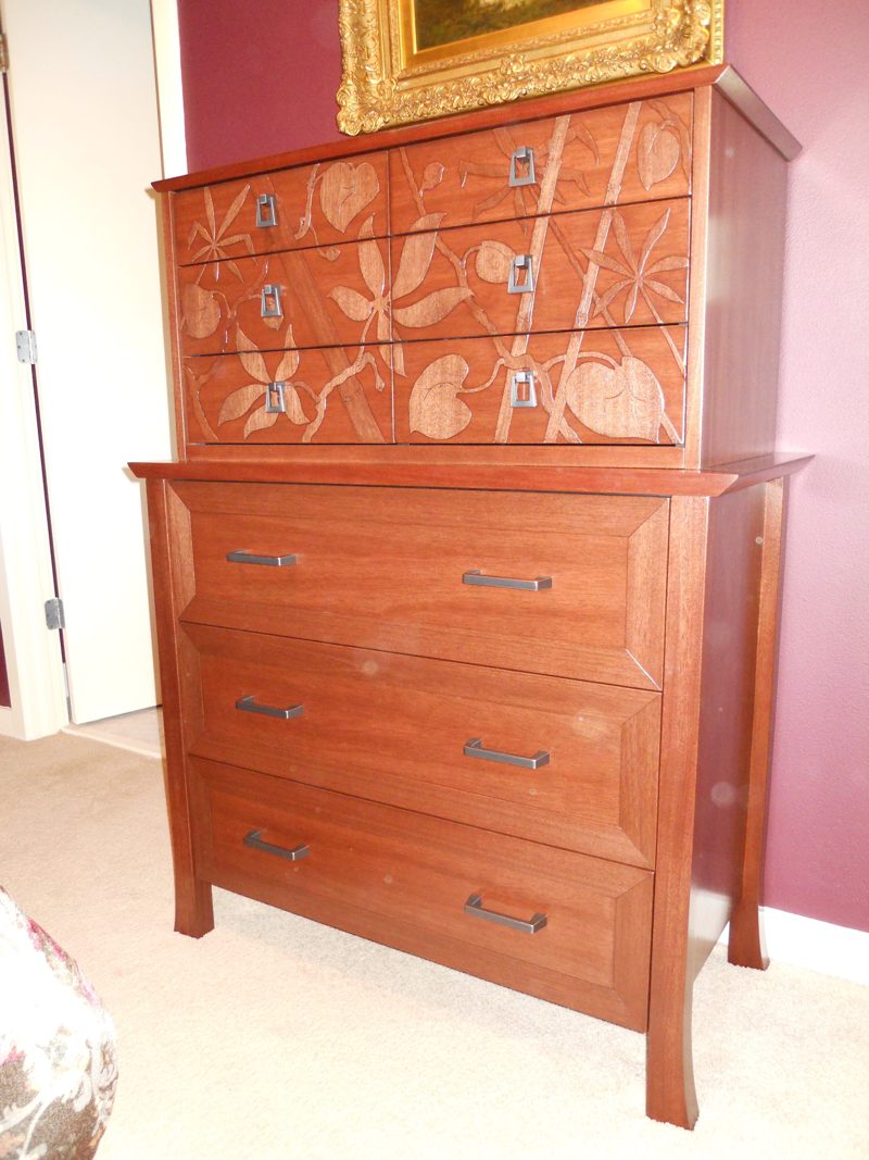 Reddish wood chest of drawers with carved leaf and vine upper drawers