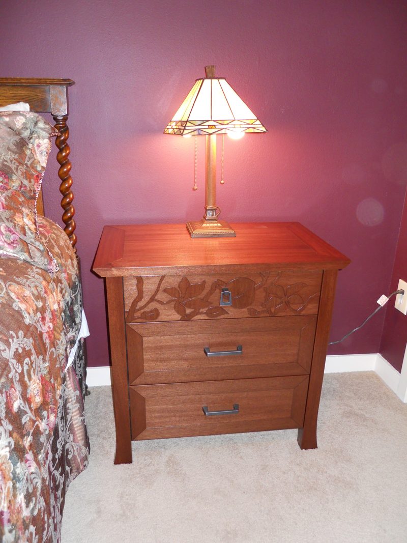 Reddish wood nightstand with carved leaves and a stained-glass lamp