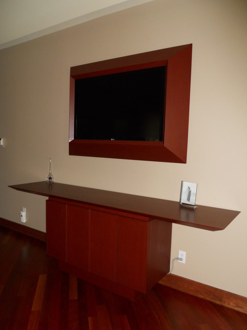 Framed wall-mounted TV above a floating reddish wood shelf and cabinet