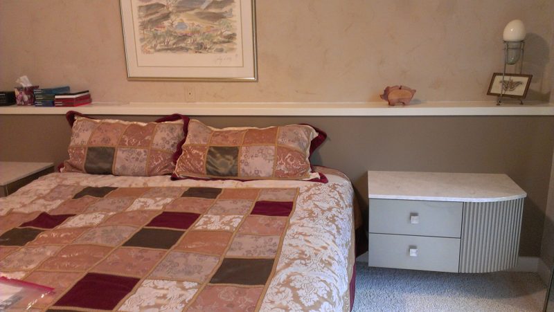 Bed with a patchwork quilt beside a gray two-drawer nightstand