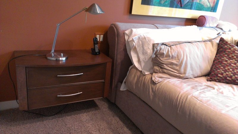 Two-drawer wood nightstand with a desk lamp beside a white sofa bed