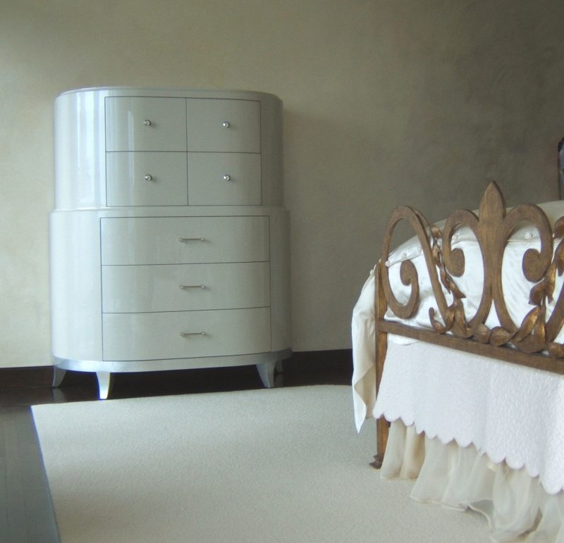 White lacquer rounded chest of drawers beside an ornate white bed