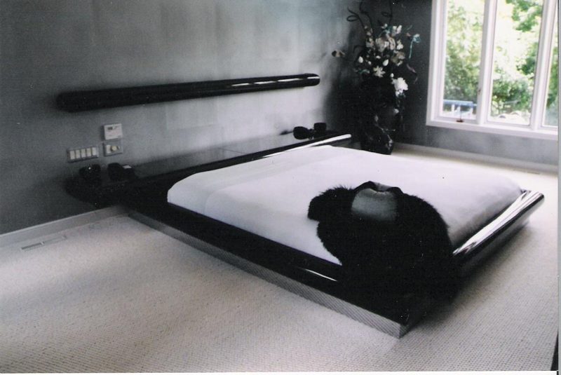 Black and white photo of a black lacquer platform bed with a floating headboard shelf