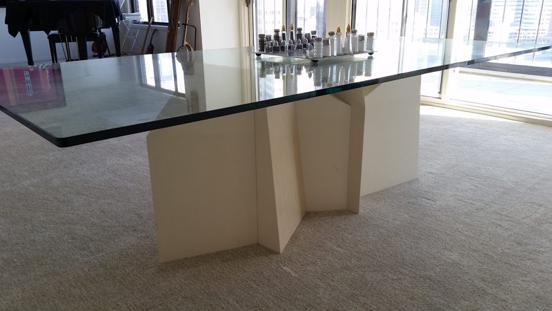 Glass dining table top resting on a sculptural cream wood pedestal base