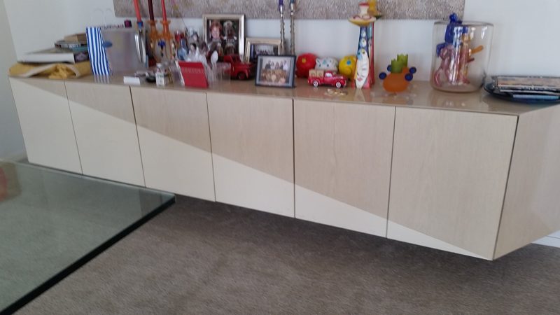 Floating light wood buffet with angled door panels beneath a long wall of decor