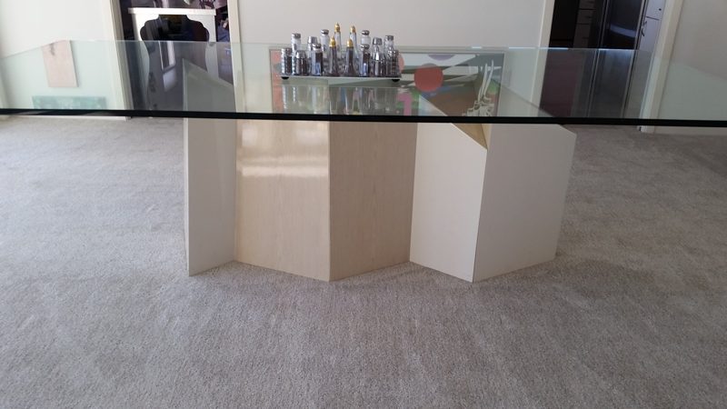 Glass-top dining table on angled light wood pedestal panels