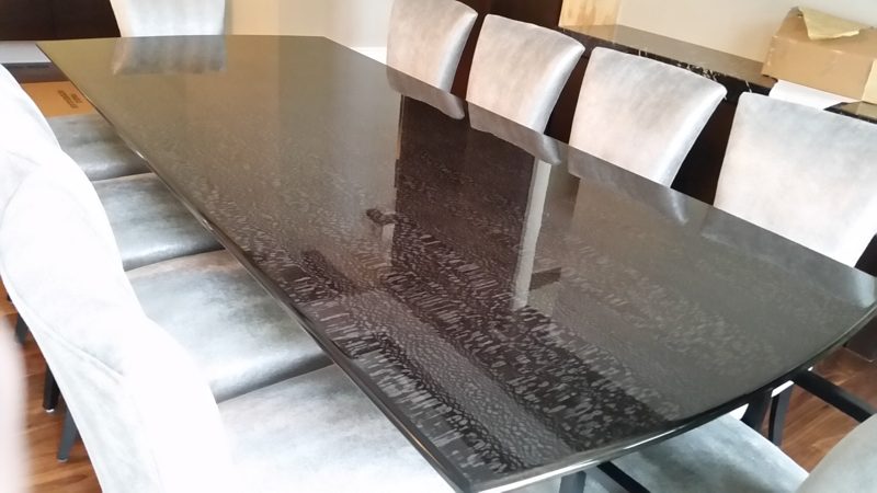Long dining table with a high-gloss dark patterned top and gray upholstered chairs