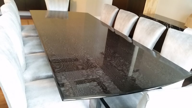 Dark patterned glossy dining table surrounded by gray upholstered chairs