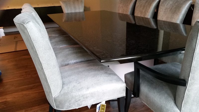 Side view of a dark gloss dining table with gray chairs and dark legs