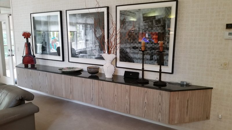 Long floating light wood-grain credenza with a dark top below framed art