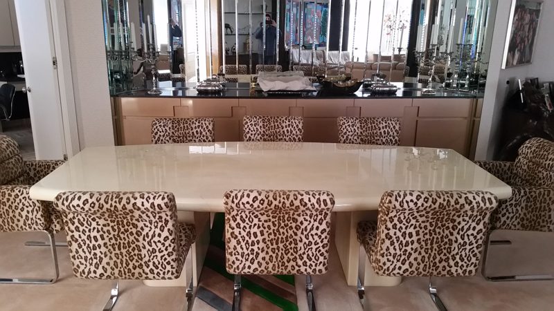 Cream lacquer dining table with animal-print chairs before a mirrored bar