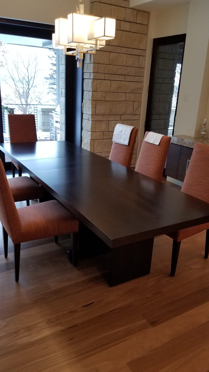 Long dark wood dining table with orange upholstered chairs by tall windows