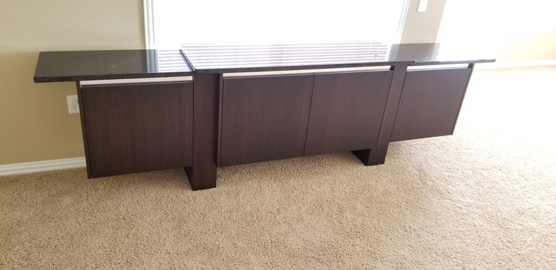 Dark wood buffet with a black top on tapered legs on light carpet