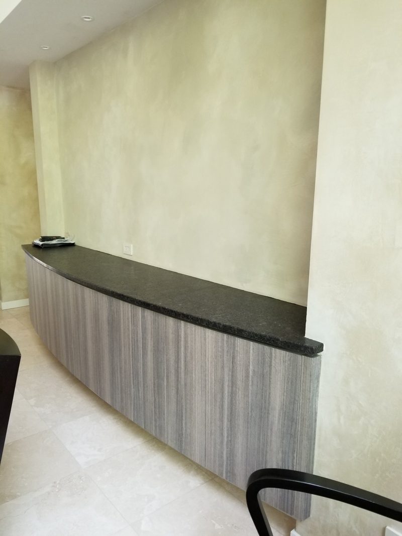 Long curved gray buffet with a black top along a plaster wall
