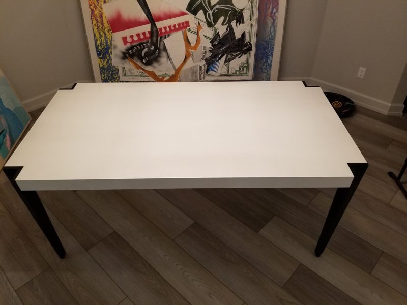 Top view of a white dining table with notched corners and black legs