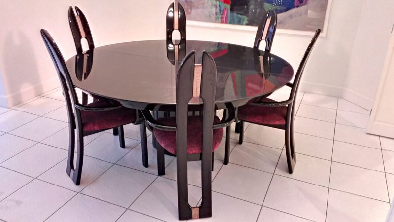 Round glossy black dining table with wood slat chairs and burgundy seats