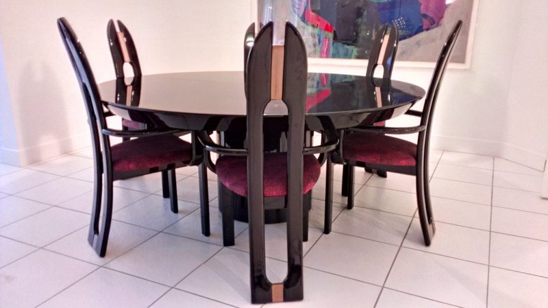Black round dining table with burgundy-seated chairs on a white tile floor