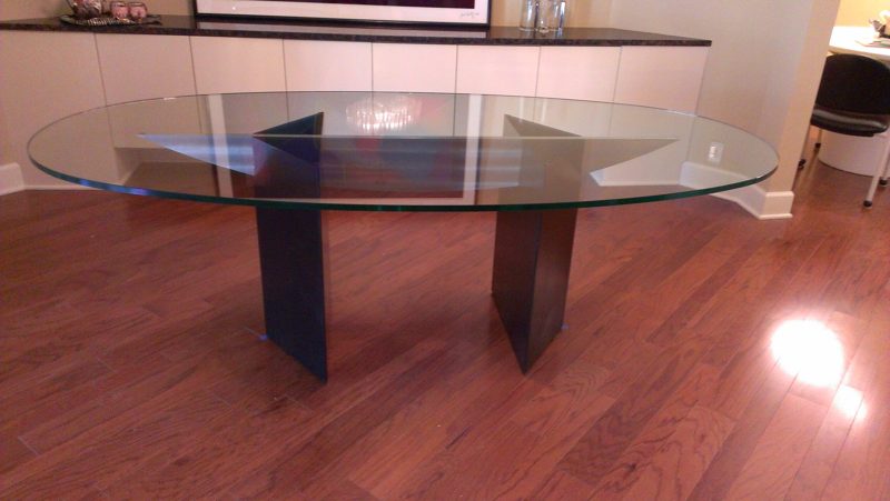 Oval glass dining table on angled black pedestal bases