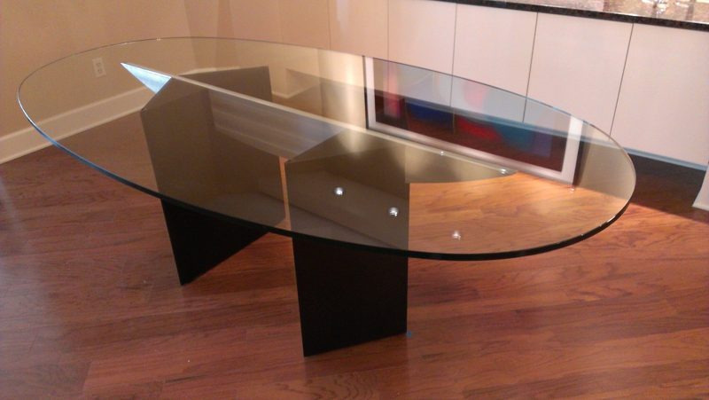 Oval glass tabletop over two black panel legs on a wood floor