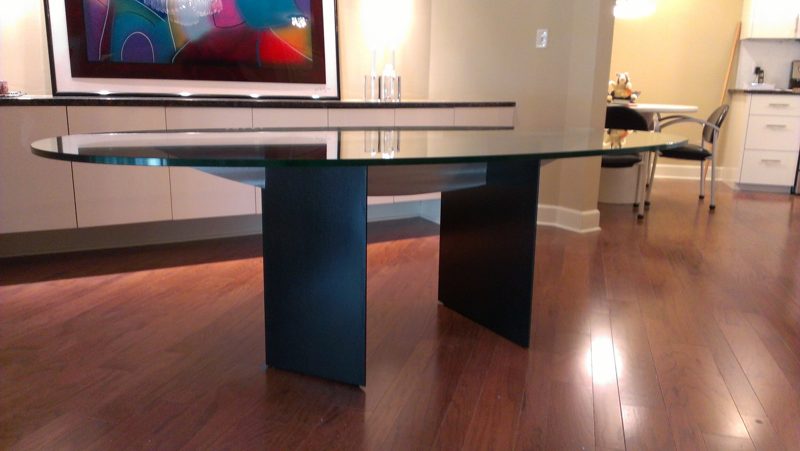 Long glass dining table on black pedestal legs below colorful art