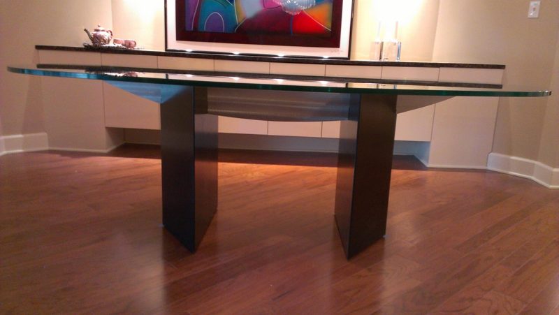 Glass-top dining table on black pedestals in front of built-in white cabinets