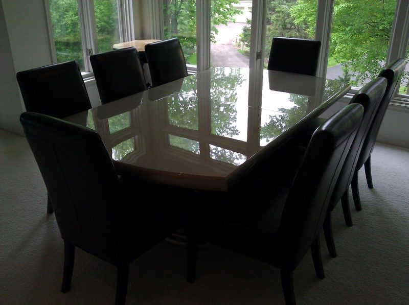 Glossy dark dining table with black leather chairs by large windows