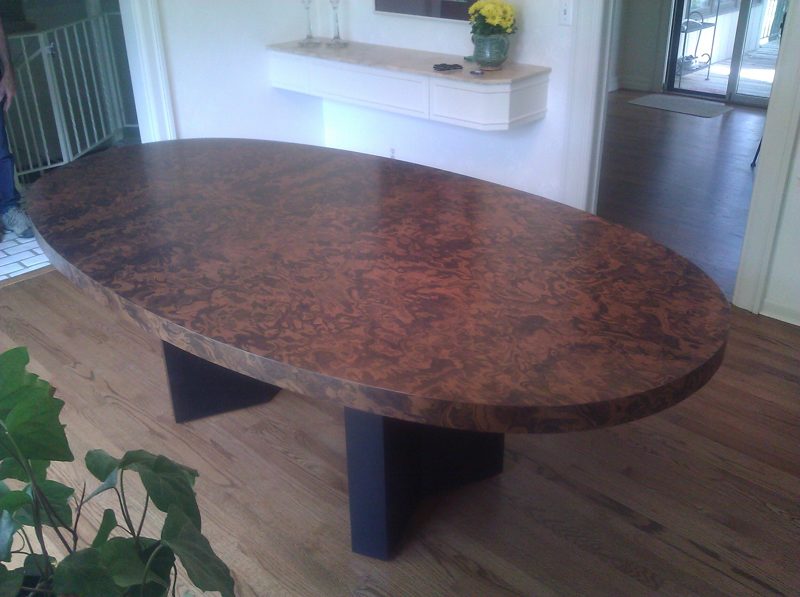 Oval burl wood dining table with a glossy finish on a dark base