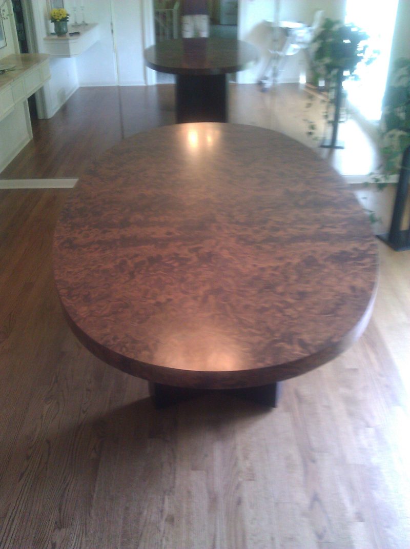 Glossy oval burl wood tabletop on a dark pedestal in a bright room