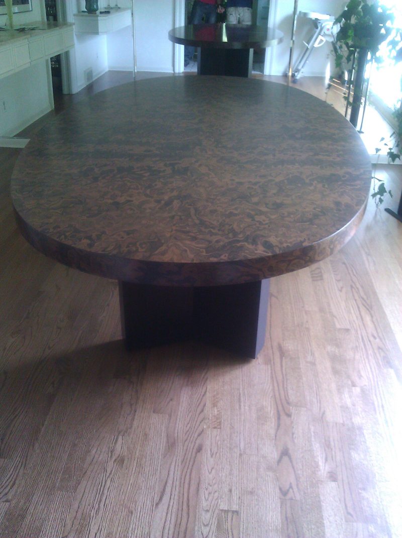 Oval burl wood dining table on a dark pedestal base on a wood floor