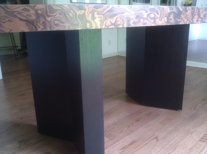 Close view of a burl wood tabletop edge over dark angled pedestal legs