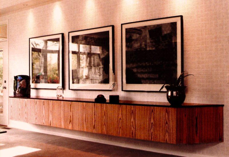 Long floating wood-grain credenza with a warm red-brown finish below framed art