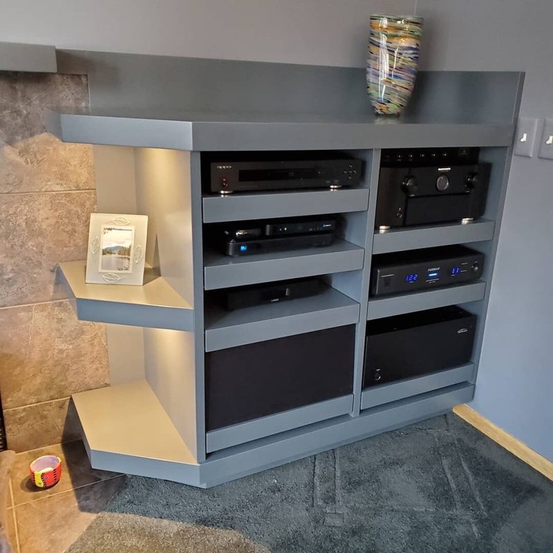 Gray media cabinet with lit open shelves holding audio equipment