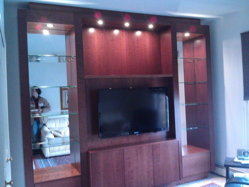 Cherry wood entertainment center with lit glass display niches and a mounted TV