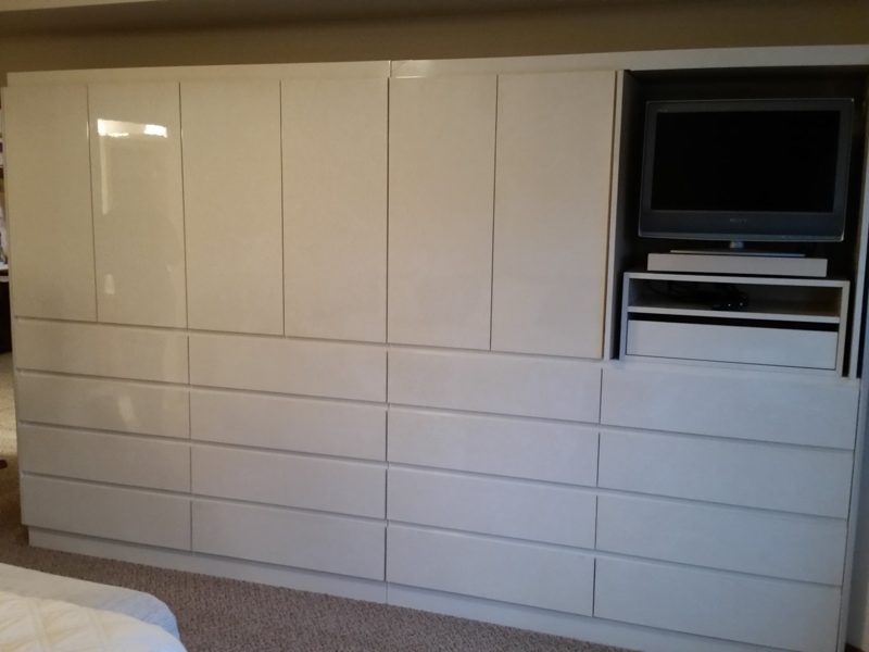 Wall of glossy white cabinets and drawers with a built-in TV niche
